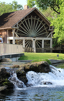 springs flowing water off rocks with people on the bridge and building behind them